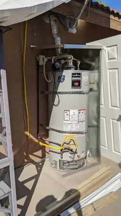 Bradford White gas water heater installed in an exterior closet alcove, yellow CSST flexible gas line visible at burner assembly, corrugated stainless connections at top, no visible corrosion, residential exterior rough-in with door enclosure.