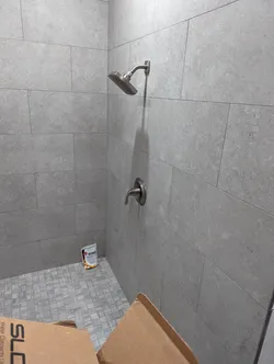 Newly tiled shower enclosure with large-format gray porcelain wall tile and mosaic floor tile, brushed nickel pressure-balance trim kit installed at standard height, tub spout arm stubbed out, no caulking or grout sealing completed yet — finish trim stage, not ready for inspection.