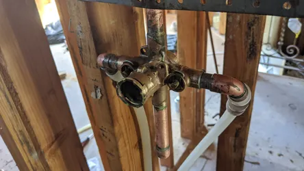 Shower valve rough-in on copper supply with heavy oxidation and verdigris on the brass mixing valve body, open stud wall remodel context, with PEX stub-outs transitioning off the copper drops — valve shows significant exterior corrosion warranting replacement before close-in.