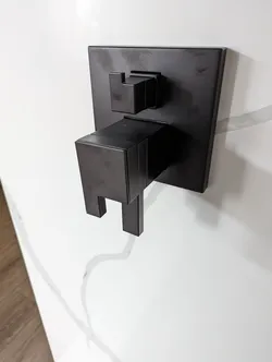 Matte black square-handle pressure-balance shower valve trim kit with integral diverter, wall-mounted on white tile surround, no visible corrosion, trim appears zinc or brass with PVD coating, concealed valve body behind wall.