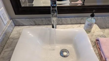 Chrome single-handle lavatory faucet with vessel-style undermount vitreous china sink on marble vanity top, chrome pop-up drain assembly, flow appears unobstructed with no visible scale, corrosion, or aerator restriction.