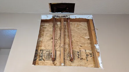 Two copper supply lines with 90-degree stub-outs are roughed in through an OSB-backed wall cavity, likely a shower or tub valve rough-in, with drywall opened for access and no visible corrosion or scale.
