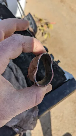 Cross-section of a copper supply line showing severe freeze damage — the pipe wall has catastrophically deformed and split outward, with heavy oxidation and scale buildup on the interior bore, consistent with a freeze-burst failure from water expansion.
